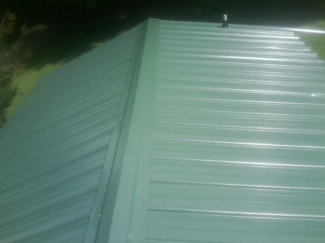 New green metal panels meeting at the ridge of a roof — Flat Roof Repair work by our crew in Proctor