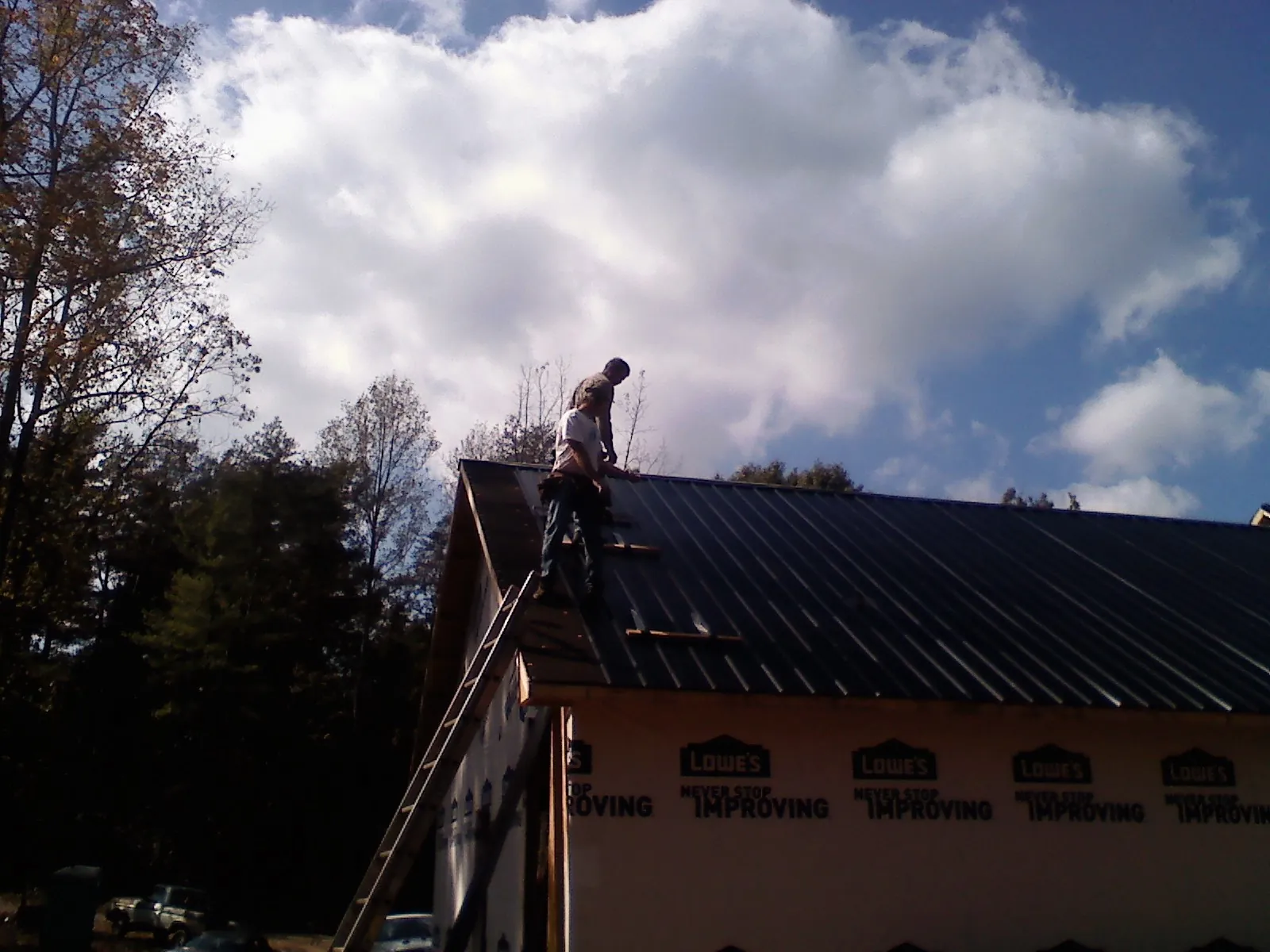 Roofer fastening dark metal panels high against a cloudy sky, from a Roof Inspection job in Proctor